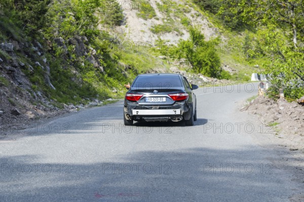 Black car driving on a winding road through the countryside, car without rear bumper, Georgia