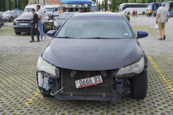 Dark car with frontal damage is parked in a parking lot with pedestrians, Georgia