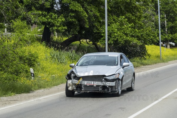 Silver car with frontal damage drives along a flower-lined road, Georgia