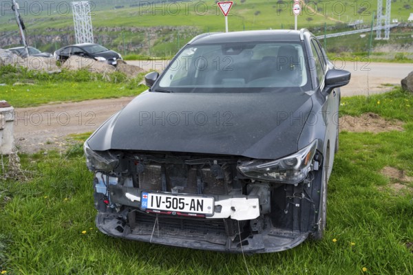 Black car with damaged front in green area on the side of the road, Georgia