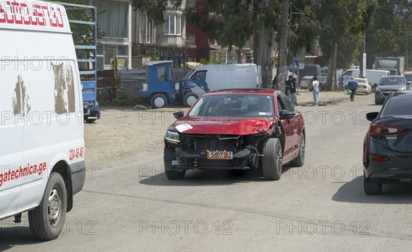 Red car with visible frontal damage on a busy road, Georgia