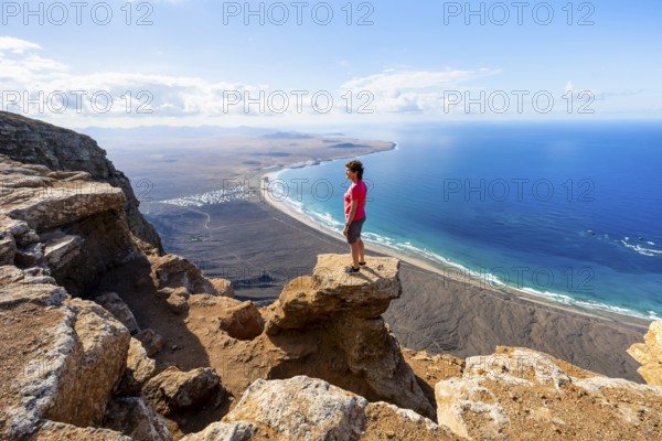 Woman enjoying the view from the Risco de Famara cliffs on Famara beach, Playa de Famara with La Calaeta, Lanzarote, Canary Islands, Spain