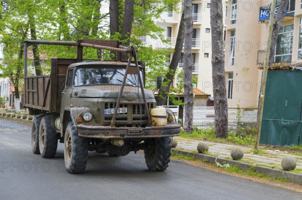 An old rustic truck is parked on a road next to tall buildings, truck ZIL -131, Ureki, Guria region, Georgia