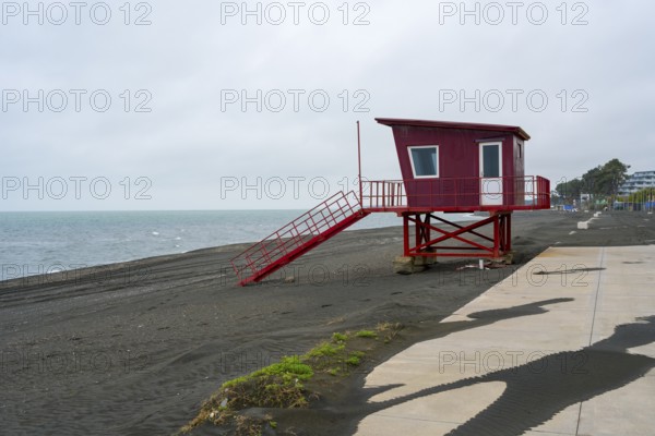 Red painted rescue tower stands abandoned on cloudy beach, beach with magnetic sand, magnetite, Ureki, Gurien region, Georgia