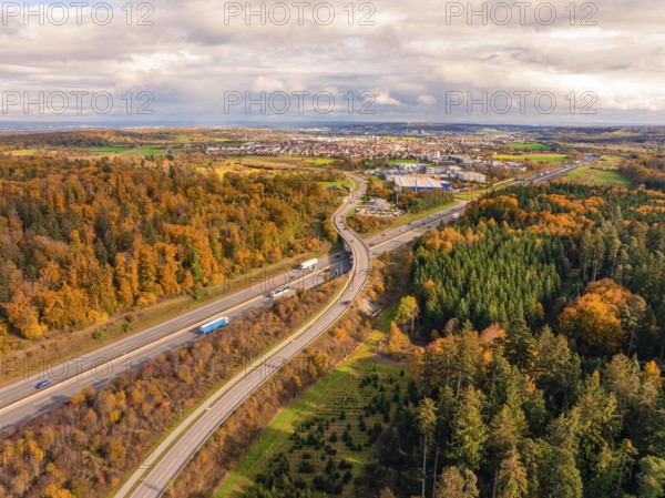 Road through autumn forest landscape with view of city in the distance and cloudy sky, A8 near Rutesheim, Germany