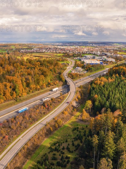 Aerial view of a road in autumn landscape with view of city and wooded area, A8 near Rutesheim, Germany