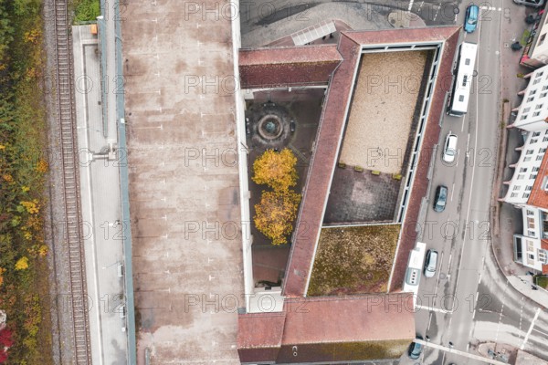 Urban aerial view with surrounding streets and buildings, a courtyard with a fountain and yellow trees visible, Hermann Hessebahn, ZOB Calw, Germany