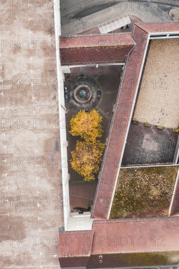 Aerial view of a courtyard with a fountain and yellow trees, surrounded by a large building with a red roof, Hermann Hessebahn, ZOB Calw, Germany