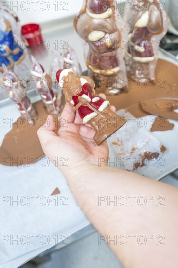 A hand holds a chocolate Santa Claus figure in a production environment, Christmas baking, Haselstaller Hof, Wildberg, Germany