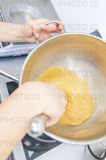 A person is stirring a yellow dough in a pan on a stove, Christmas baking, Haselstaller Hof, Wildberg, Germany