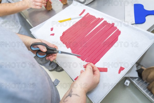 Red strips are cut with scissors on a baking sheet, Weihnachtsbacken, Haselstaller Hof, Wildberg, Germany