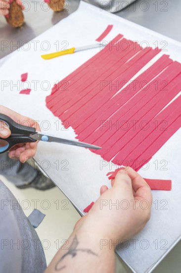 Hand cuts red paper strips with scissors on baking tray, Christmas baking, Haselstaller Hof, Wildberg, Germany