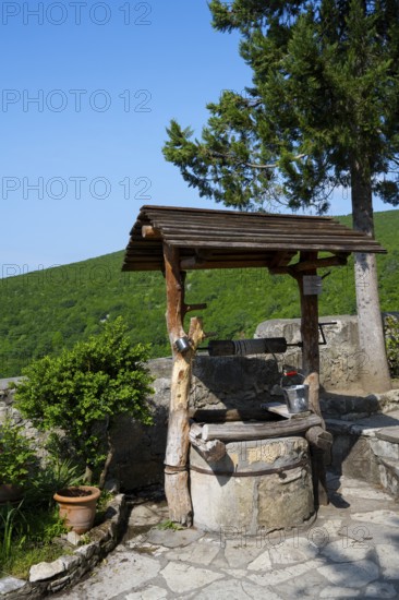 Rustic fountain with wooden roof surrounded by nature and plants in sunny weather, Motsameta monastery, near Kutaisi, Imereti region, Georgia