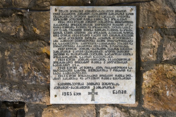 A plaque on a stone wall inscribed with religious text, a cross below, memorial plaque dedicated to the Georgian poet Galaktion Tabidze, Motsameta monastery, near Kutaisi, Imereti region, Georgia
