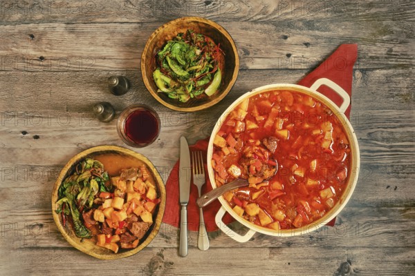 A large pot of beef stew on a wooden tabletop. Portion of beef stew is served on a rustic wooden plate and a glass of red wine create a cozy dining scene emphasising the simple life and nutritious nourishment