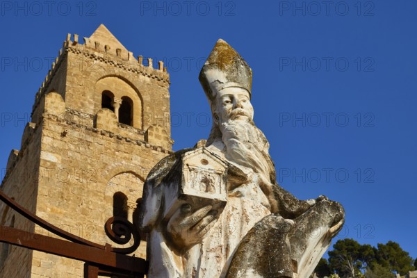 Stone statue of a saint in front of a tower against blue sky, symbolizing historical strength of faith, Cefalu, cathedral, UNESCO World Heritage Site, Sicily, Italy