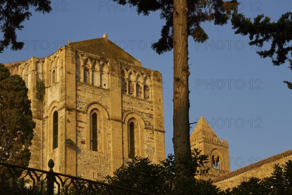 Detail of the steeple of a Romanesque church in warm sunlight, surrounded by trees, Cefalu, cathedral, UNESCO World Heritage Site, Sicily, Italy