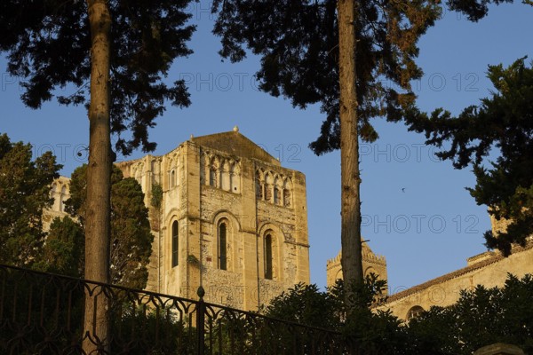 Historic Romanesque church surrounded by trees under clear blue sky at sunset, Cefalu, cathedral, UNESCO World Heritage Site, Sicily, Italy