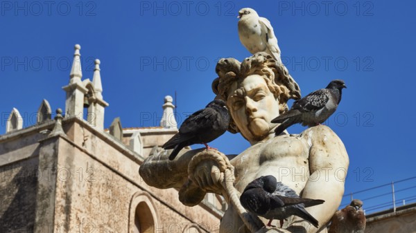 Marble sculpture with doves under a blue sky, in the background historic baroque style building, Monreale, cathedral, UNESCO World Heritage Site, Sicily, Italy
