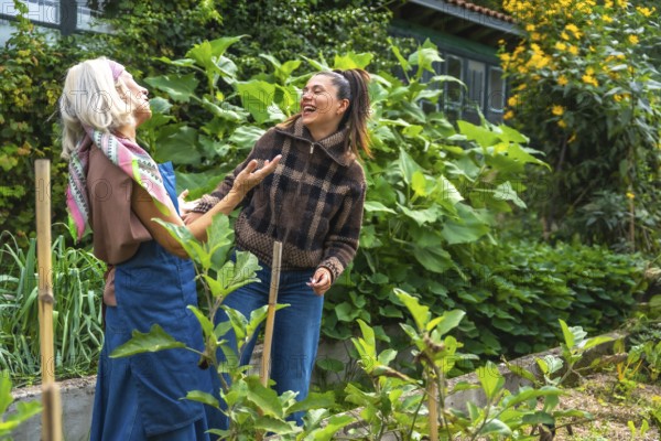 Two cheerful women of different generations are laughing and bonding outdoors, tending to plants in a vibrant home garden, sharing a joyful moment of connection and healthy lifestyle