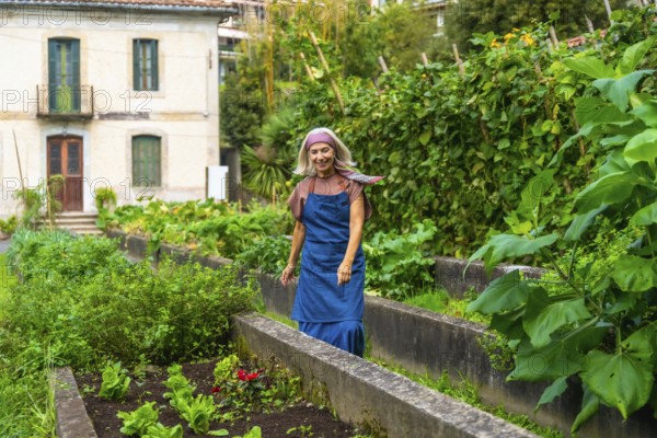 Senior woman smiling while walking through her bountiful urban vegetable garden, cultivating fresh organic produce in raised beds, embracing a sustainable lifestyle
