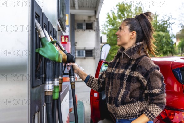 Woman in a casual plaid jacket holding a fuel pump nozzle, refueling her red car at a gas station, symbolizing transportation, energy consumption, and daily life