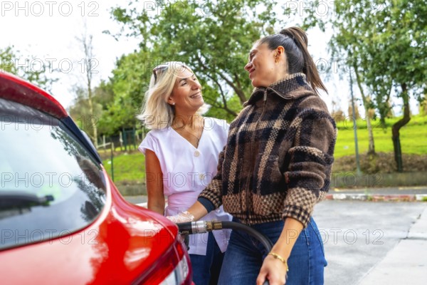 Mother smiling as daughter fills the red car with fuel at a gas station, sharing a warm moment of guidance, learning and family bonding during a road trip stop