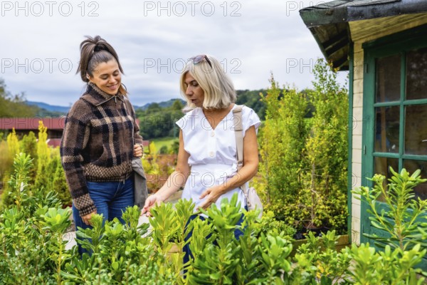 Two women, a mother and daughter, enjoying a shared activity outdoors, carefully selecting plants for their garden from a wide variety available at a plant nursery