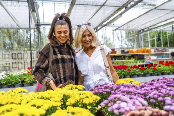 Happy mother and adult daughter enjoying choosing colorful blooming flowers together, bonding and spending quality time while shopping in a bright garden center greenhouse