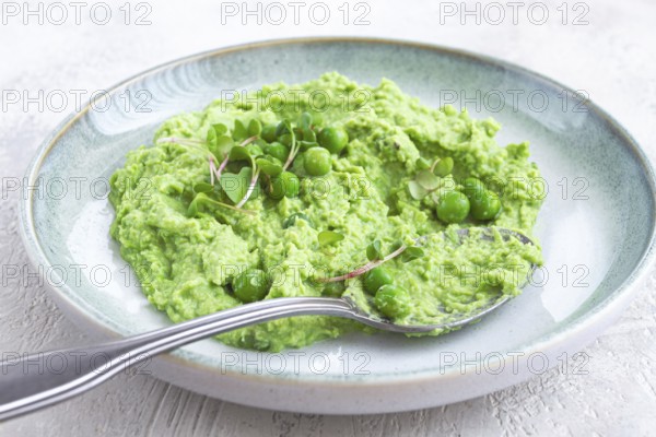A vibrant green pea puree fills a shallow bowl, topped with fresh peas and microgreens. The dish looks fresh and inviting, ideal for a light, nutritious meal at any time