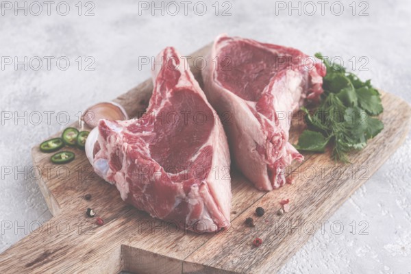 Fresh pieces of beef on the bone, on a wooden cutting board, with herbs and spices, ready for cooking in the kitchen