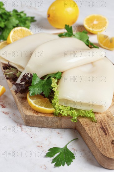 Fresh squid prepared for cooking, surrounded by herbs and lemon, placed on a wooden chopping board in a bright kitchen setting