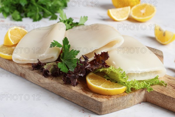 Fresh squid prepared for cooking, surrounded by herbs and lemon, placed on a wooden chopping board in a bright kitchen setting