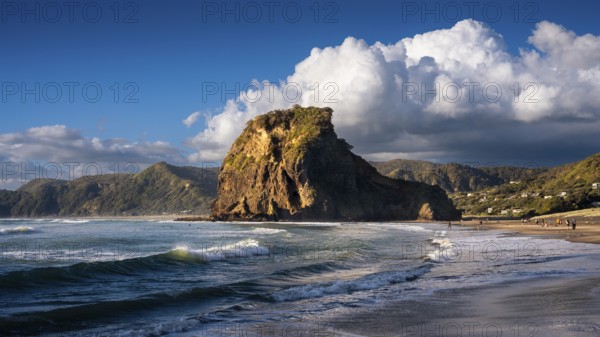 Landscape in New Zealand with sea and sandy beach. Piha Beach and Lion Rock. People on the beach, surfers in the water. Piha, Waitakere Ranges, West Auckland, New Zealand
