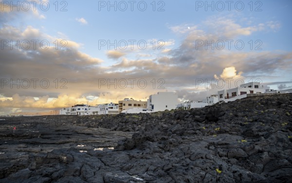 Black coast of volcanic rocks behind typical white houses of the village of La Santa, at sunset, Lanzarote, Canary Islands, Spain
