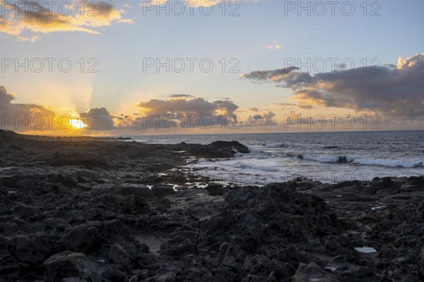 Dramatic cloudy sky with sunbeams at sunset, seaside coast with volcanic rocks, La Santa, Lanzarote, Canary Islands, Spain