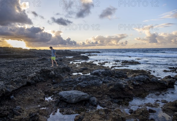 Tourist strolling on seaside coast with volcanic rocks at sunset, La Santa, Lanzarote, Canary Islands, Spain