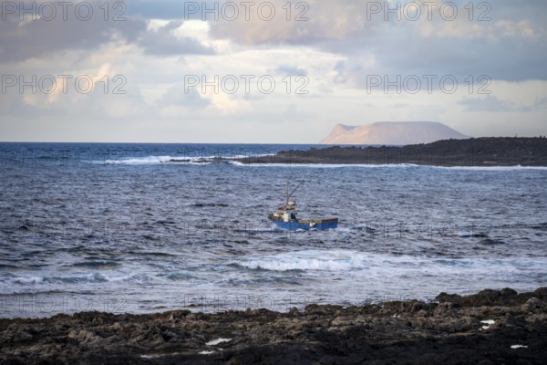 Fishing boat out to sea in the evening, seaside coast with volcanic rocks at sunset, La Santa, Lanzarote, Canary Islands, Spain