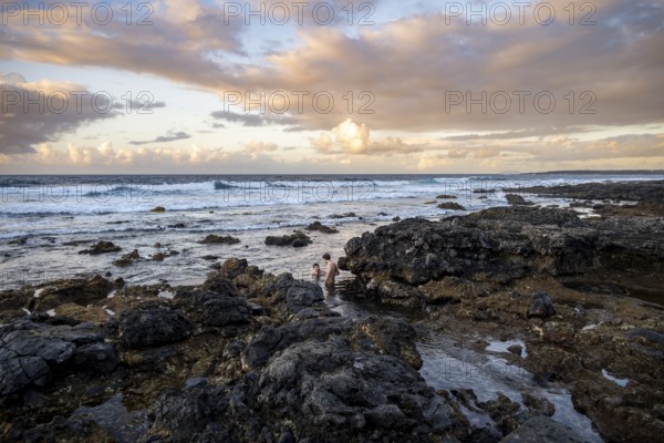 Tourists swim in the sea on rocky coast at sunset, La Santa, Lanzarote, Canary Islands, Spain