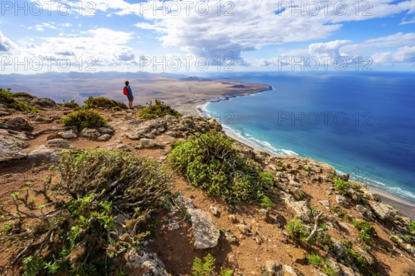 Tourist at Castillejo viewpoint, view from the Risco de Famara cliffs of the coast and the sea with the Famara beach, Playa de Famara, Lanzarote, Canary Islands, Spain
