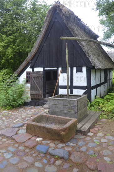 Older half-timbered house with thatched roof by older well in Den gamle by, The old village, open air museum in Odense, Fyn island, Fuen, Denmark, Scandinavia