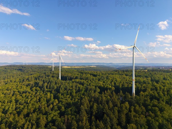 Three wind turbines stand in a green forest landscape under a clear sky, near Schorndorf, Rems-Murr-Kreis, Baden-Württemberg, Germany
