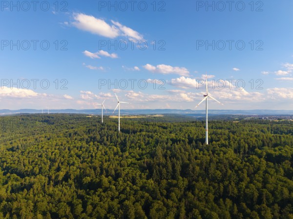 Several wind turbines rise above a lush forest under a sky with light clouds, near Schorndorf, Rems-Murr-Kreis, Baden-Württemberg, Germany