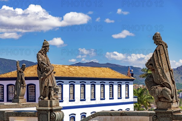 Statues of biblical prophets sculpted by Aleijadinho with ancient buildings and mountains in the background in Congonhas, Minas Gerais