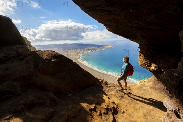 Tourist in the Cueva de las Cabras cave, woman enjoying the view from the Risco de Famara cliffs on Famara beach, Playa de Famara with La Calaeta, Lanzarote, Canary Islands, Spain