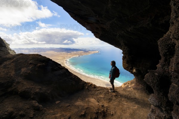 Tourist in the Cueva de las Cabras cave, old woman enjoying the view from the Risco de Famara cliffs on Famara beach, Playa de Famara with La Calaeta, Lanzarote, Canary Islands, Spain