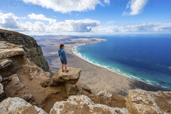 Woman enjoying the view from the Risco de Famara cliffs on Famara beach, Playa de Famara with La Calaeta, Lanzarote, Canary Islands, Spain