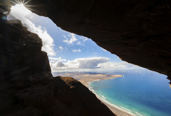 Cueva de las Cabras cave, view from the Risco de Famara cliffs to Famara beach, Playa de Famara with La Calaeta, sun stars, Lanzarote, Canary Islands, Spain