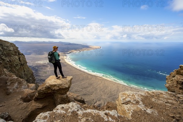 Young woman enjoying the view from the Risco de Famara cliffs to Famara beach, Playa de Famara with La Calaeta, Lanzarote, Canary Islands, Spain