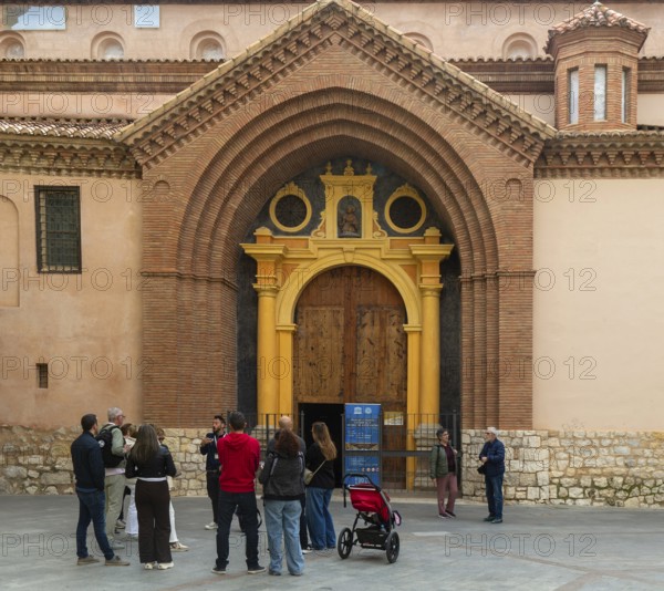 Tour guide and group of people outside Mudéjar door of cathedral church building, city centre of Teruel, Aragon, Spain